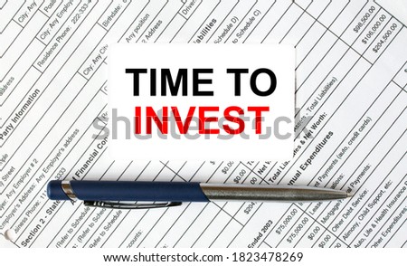 Text Time To Invest written on a business card lying on financial tables with a blue metal pen. Business and financial concept