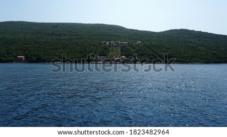 View of the mountain coastline covered with dense green forest. Blue and calm sea. Clear and blue sky. Summer sunny day. Picturesque landscape.                              