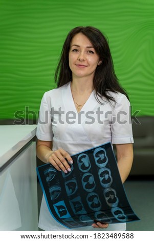 Doctor holding an x-ray image near the white table. Magnetic resonance imaging film. Medic in scrubs.
