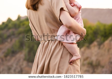 A young mother stands looking at the quarry or mountains and holds a child in her arms. Sunset. Close-up, view from the back. Active lifestyle. Travels Royalty-Free Stock Photo #1823517785
