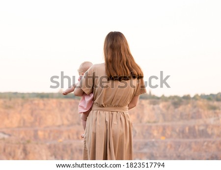 A young mother stands looking at the quarry or mountains and holds a child in her arms. Sunset. Close-up, view from the back. Active lifestyle. Travels Royalty-Free Stock Photo #1823517794