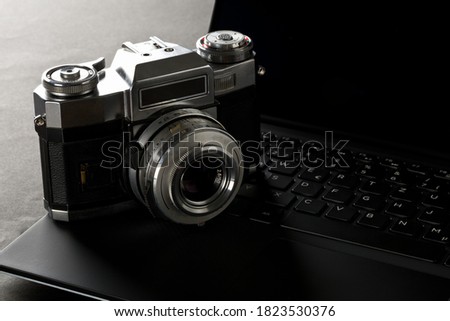 Retro analog SLR camera on laptop keyboard on black desk in office, digital photography or image processing concept, selective focus