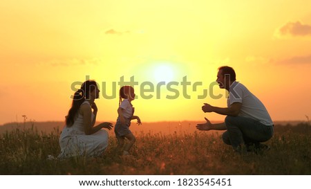 little daughter goes from mom to dad, hugs and kisses her parents in rays of warm sun. Happy family walks in park at sunset. Mom, dad and baby. healthy family plays in field. Happy family concept