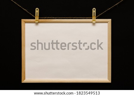 A wooden frame hangs on a rope with clips, clothes. Frame on a black background with a white space for dough, advertising or photo. horizontal photo.