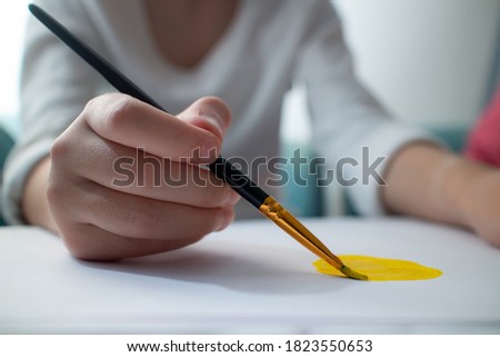 Child's hand draws yellow sun on white paper. Drawing lessons at school. Home schooling. Art. Close-up of a brush. High quality photo