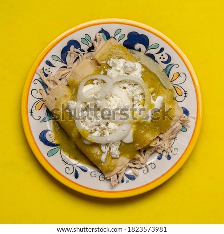 Traditional mexican green enchiladas with chicken and cheese on yellow background