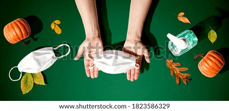Person holding a mask with autumn pumpkins and leaves - healthcare and hygiene concept