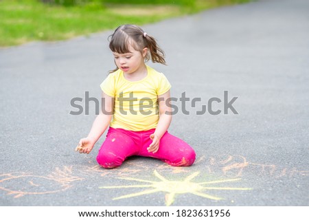 Girl with syndrome down draws the sun with chalk on the asphalt 