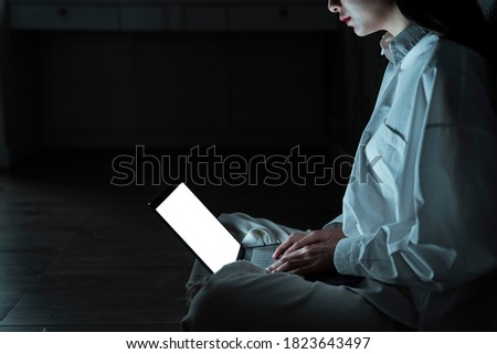 Cropped image of laptop is used ny the woman in white clothes in the dark room.