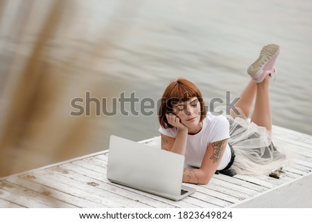 Content writer thinking text on laptop while lying on pier with closed eyes
