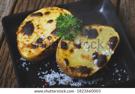Cut and Grilled potato with salt seasoning ingredient on wooden plate.