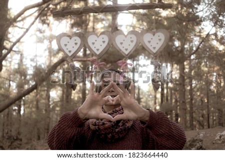 A mature woman expresses her love for nature by forming a heart with her hands in the forest. Human hands in the twilight light in the autumn season