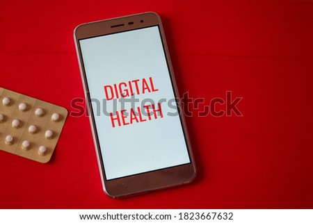 Close-up of a mobile phone with the message DIGITAL HEALTH laid on red background with medications. Virtual healthcare and medical concept.