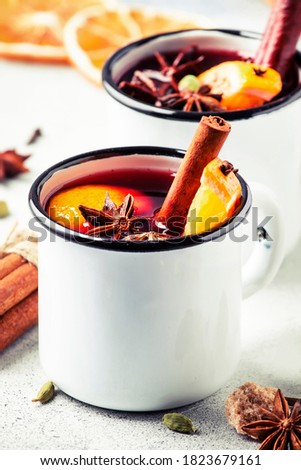 Mulled wine in white metal mugs with cinnamon, spices and orange on gray background, traditional drink on winter holiday. Copy space 