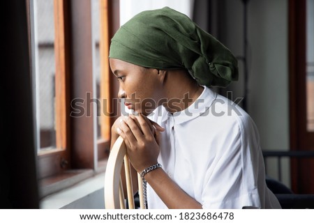 Portrait of sad African young woman cancer patient fighting with the sickness, wearing head scarf after suffering serious hair loss side effect due to chemotherapy, concept of cancer awareness Royalty-Free Stock Photo #1823686478