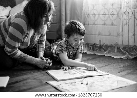 Woman reading a book with her little son sitting on the floor in home. Black and white photo.