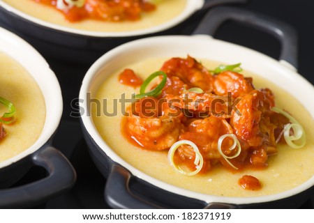 Spicy Prawns & Polenta - Soft polenta topped with prawns in tomato and chili sauce garnished with spring onion. Black background with reflections.