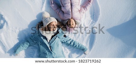 Top view portrait of cheerful mother with small daughter lying in snow in winter nature. Royalty-Free Stock Photo #1823719262