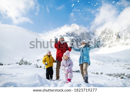 Father and mother with two small children in winter nature, playing in the snow.