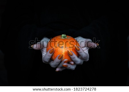 Happy Halloween theme. Small pumpkin in witches pale knotty hands with sharp long nails, low key, selected focus. Samhain, witchcraft, magic, pagan, sorcery, spell and tradition concept