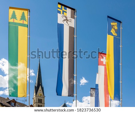 Colorful flags of Switzerland, the canton of Grisons and Val Müstair in Santa Maria, with the church tower in the background