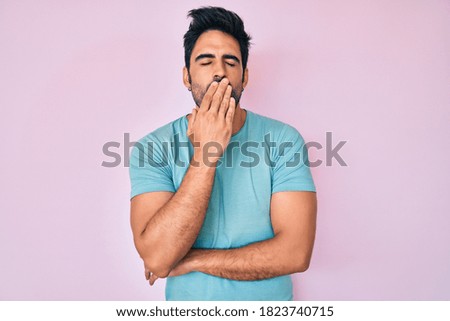 Handsome hispanic man with beard wearing casual clothes bored yawning tired covering mouth with hand. restless and sleepiness. 