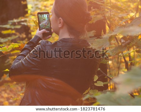 a young woman takes photos of nature on her smartphone. Sunny autumn in the Park. strolls.