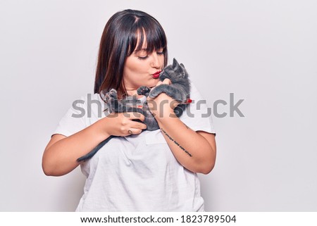 Young beautiful plus size woman smilling happy and confident. Standing with smile on face holding and kissing adorable cat over isolated white background
