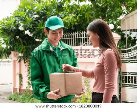 Delivery man who wearing green uniform with cap smile and hold parcel box for consumer girl sign autograph to accept online order in smartphone application by stylus pen at home local area