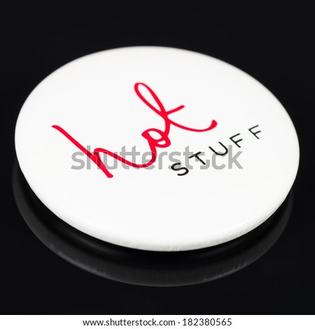 Magnetic white button with the expression 'hot stuff' written on it on a black background with reflections.