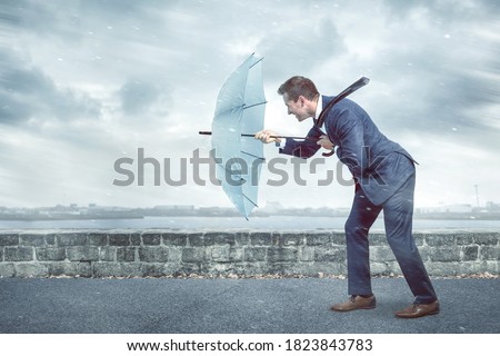Businessman with an umbrella is facing strong headwind Royalty-Free Stock Photo #1823843783