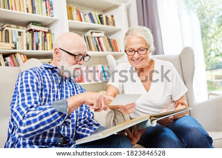 Couple of seniors with dementia look at photo album as a reminder in the living room of the nursing home