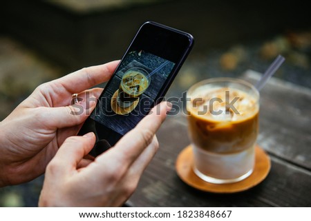 A person is taking a picture of iced latte in a coffeehouse with their smartphone