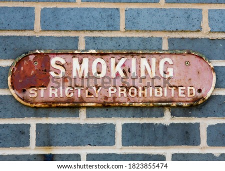 Road Sign on a brick wall reading  "Smoking is strictly forbidden."
