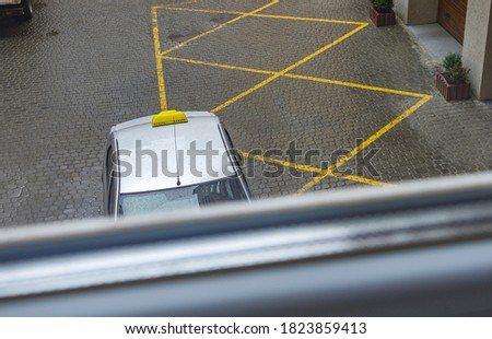 A taxi near the entrance to an apartment building is waiting for a passenger in rainy, cloudy weather. View through the window.