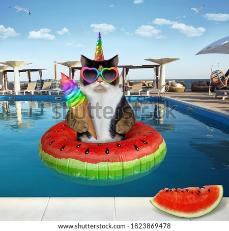 A cat unicorn in sunglasses is eating an ice cream cone with watermelon in a swimming pool at a beach resort.