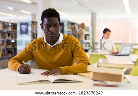 Intelligent african-american male student engaged in research working with books in university library. High quality photo