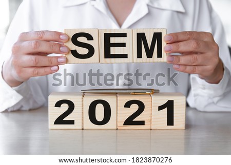 SEM 2021 - text on wooden cubes on a wooden table. Hands of businesswoman as the background. Business financial concept.