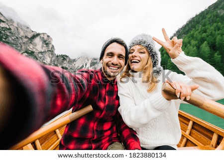 Romantic couple of adults in love taking a selfie on a boat visiting an alpine lake at Braies Italy at autumn fall. Couple, wanderlust and travel concept. Cold colours.