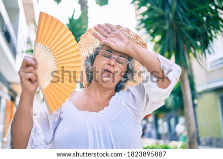 Middle age woman with grey hair using handfan on a very hot day of a heat wave Royalty-Free Stock Photo #1823895887