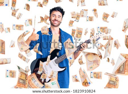 Young hispanic man playing electric guitar smiling happy and positive, thumb up doing excellent and approval sign