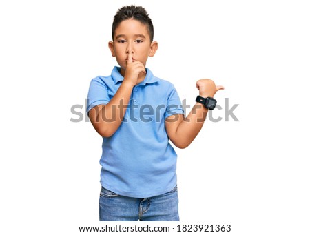 Little boy hispanic kid wearing casual clothes asking to be quiet with finger on lips pointing with hand to the side. silence and secret concept. 