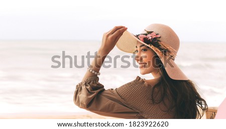 Happy smile young adult asian woman relax at beach on day. Wearing dress cloth and sun hat. Holidays domestic travel for wellness lifestyle concept. Background with copy space.