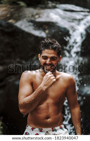 A Caucasian young male wet from swimming in a waterfall pool