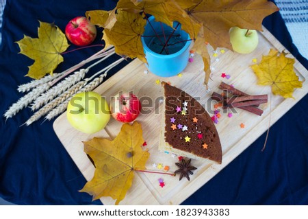 Cupcake decorated with confectionery colored sugar stars, cinnamon, autumn leaves, apples and ears of wheat on a wooden cutting board, top view