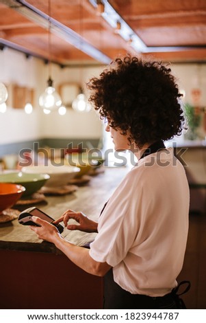Back view of waitress working with a card terminal. Woman with apron standing behind the bar counter of a restaurant. Small business owner, young entrepreneur conceptual.