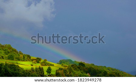 The bright sun creates a rainbow over the hill, a few moments after heavy rain