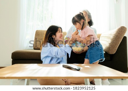 Asian niece and grandma are enjoying in their living rooms in their homes. Are enjoying eating popcorn