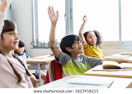 Diversity of elementary school students raise their hands to answer teacher questions. Back to school concept Royalty-Free Stock Photo #1823958215