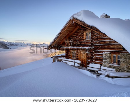 Snow covered mountain hut old farmhouse in the ski region of Saalbach Hinterglemm in the Austrian alps at sunrise against blue sky Royalty-Free Stock Photo #1823973629